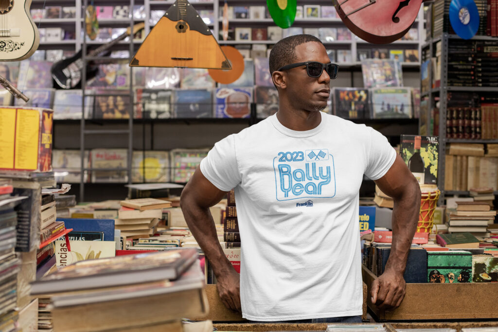 White T-shirt mockup featuring a 2023 Rally Year graphic on a model in a record shop.